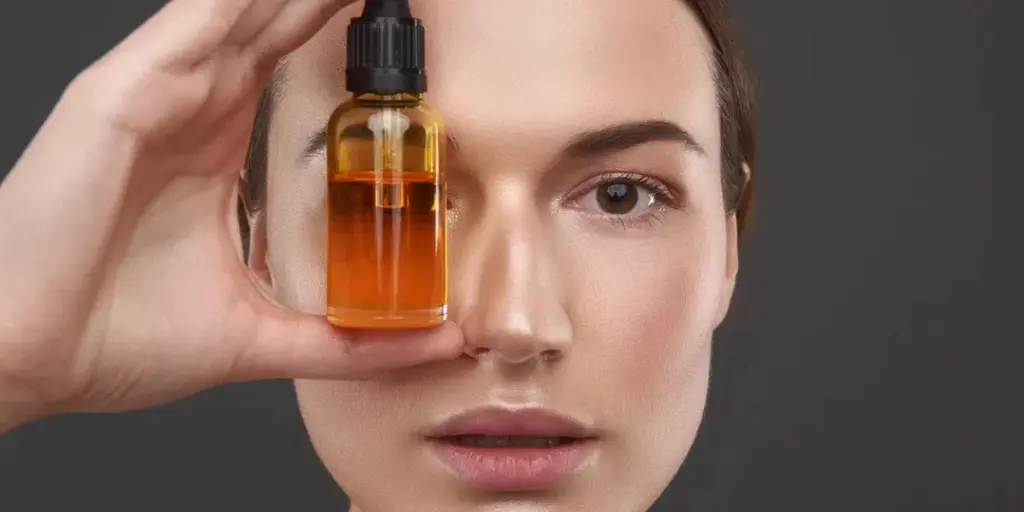 Close-up-portrait-of-smiling-lady-holding-bottle-of-orange-serum-and-making-funny-face.webp